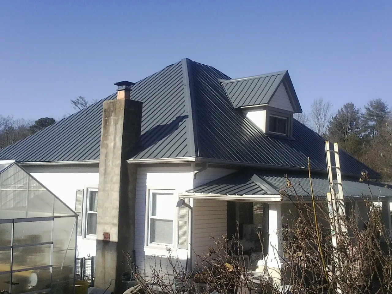 Dark blue standing seam metal roof on a white farmhouse with dormer — Slate & Tile Roof Repair by Roofing Brothers in Spring Creek