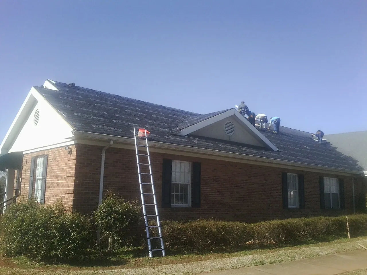 Crew tearing shingles off a brick ranch roof with a ladder set — Metal Roof Repair work by our crew in Spring Creek