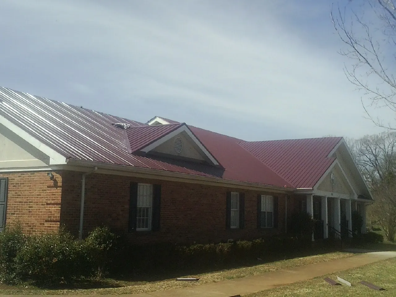 Red metal roof with gabled entries on a long brick building, from a Hail Damage Roof Repair job in Spring Creek
