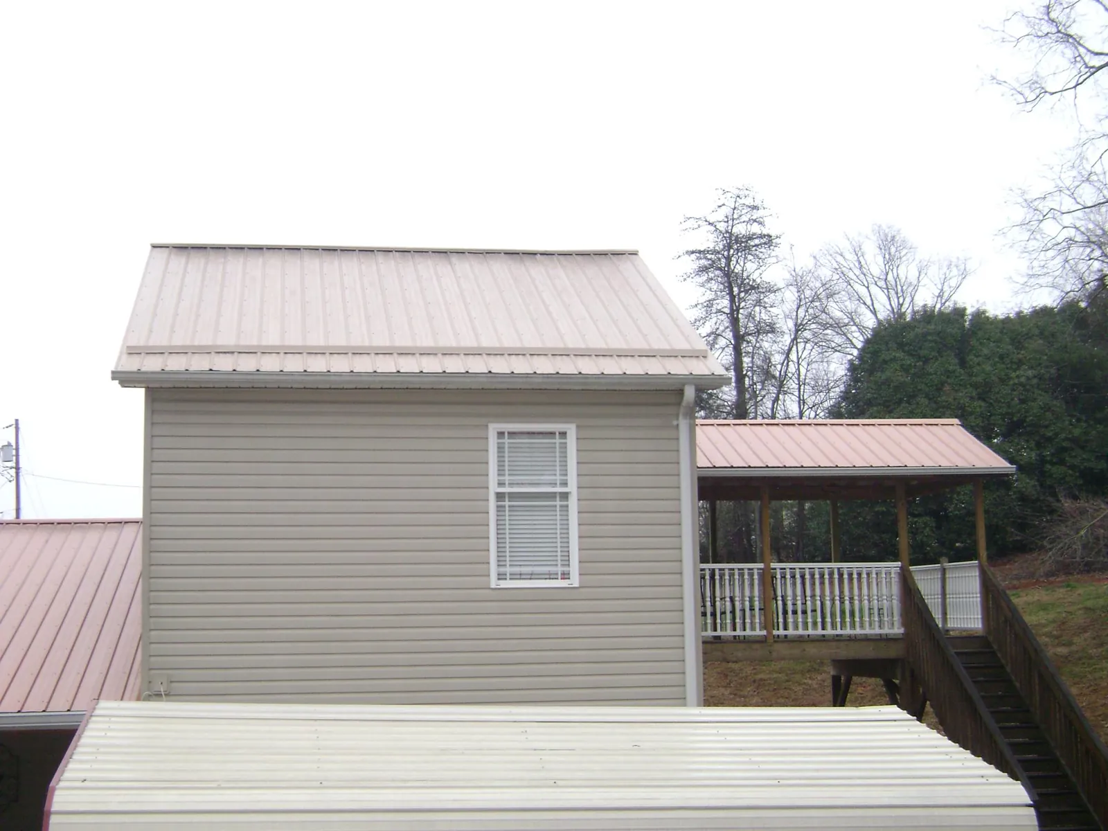 Tan metal roofs on a two story addition and attached porch, from a Roof Replacement job in Spring Creek